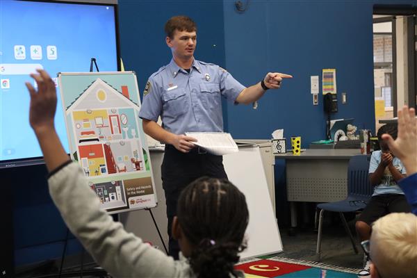  A firefighter points to a student. There's a student with their hand raised in the foreground.