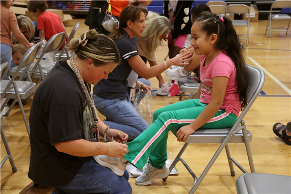 A woman kneels down to tie a girl's new pair of shoes.