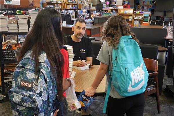  Author Jarrett Lerner sits behind a table ready to sign book, looking up at two girls.