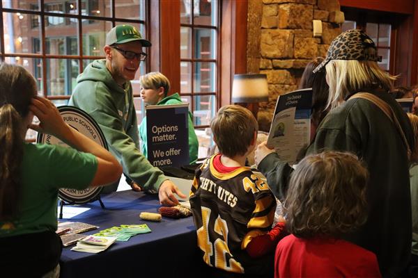  A man reaches across a table display to show something to a woman and two kids in front of him. 