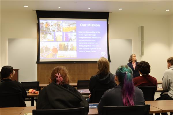 Students look away from the camera at a screen stating Crossline's mission. A woman talks to them.