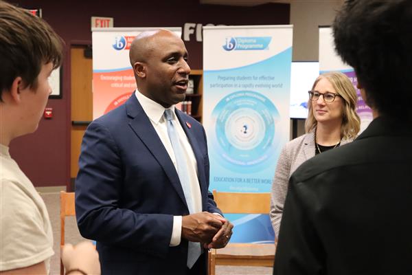 Mayor Lucas stands in front of some IB posters talking with students and staff.