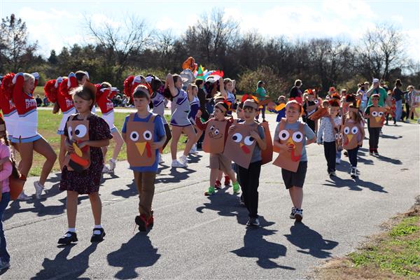  Students dress as turkeys walk a track with cheerleaders in the background.