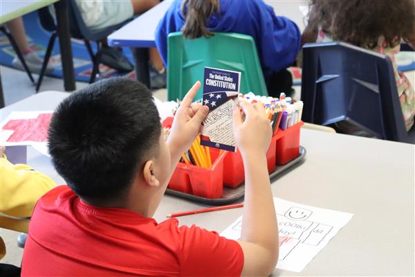 A male student in a red shirt holds up a copy of the U.S. Constitution.