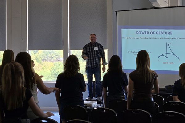 Dr. Nathan Cornelius stands in front of a crowd next to a screen title's power of gesture.